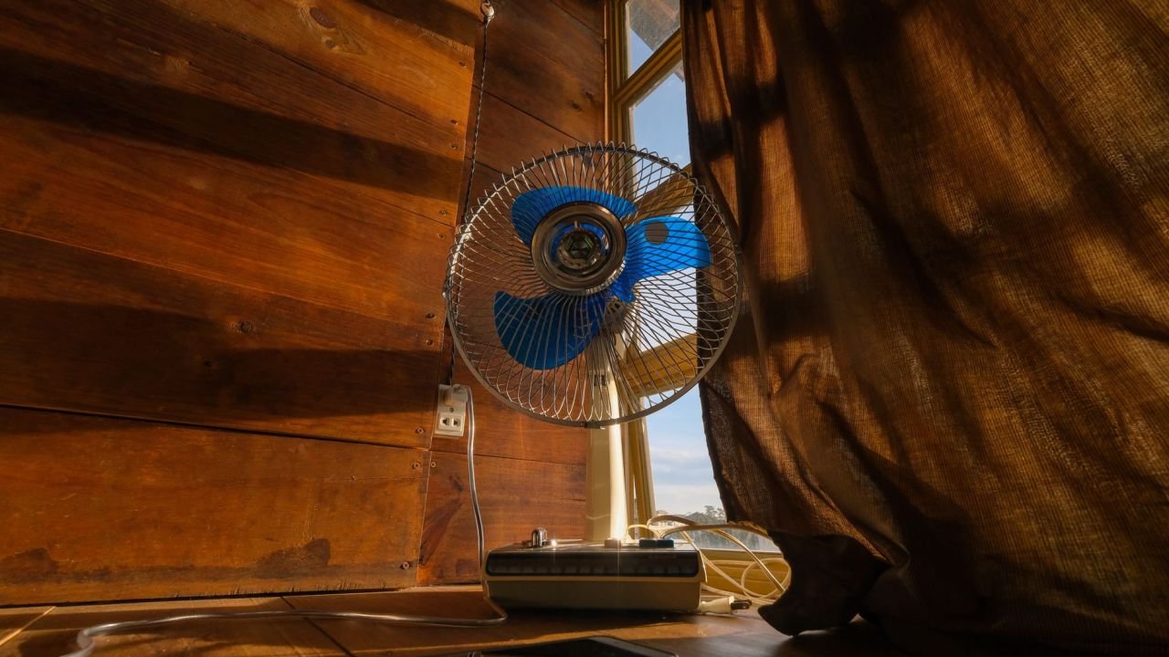 An electric fan beside a sunlit curtain