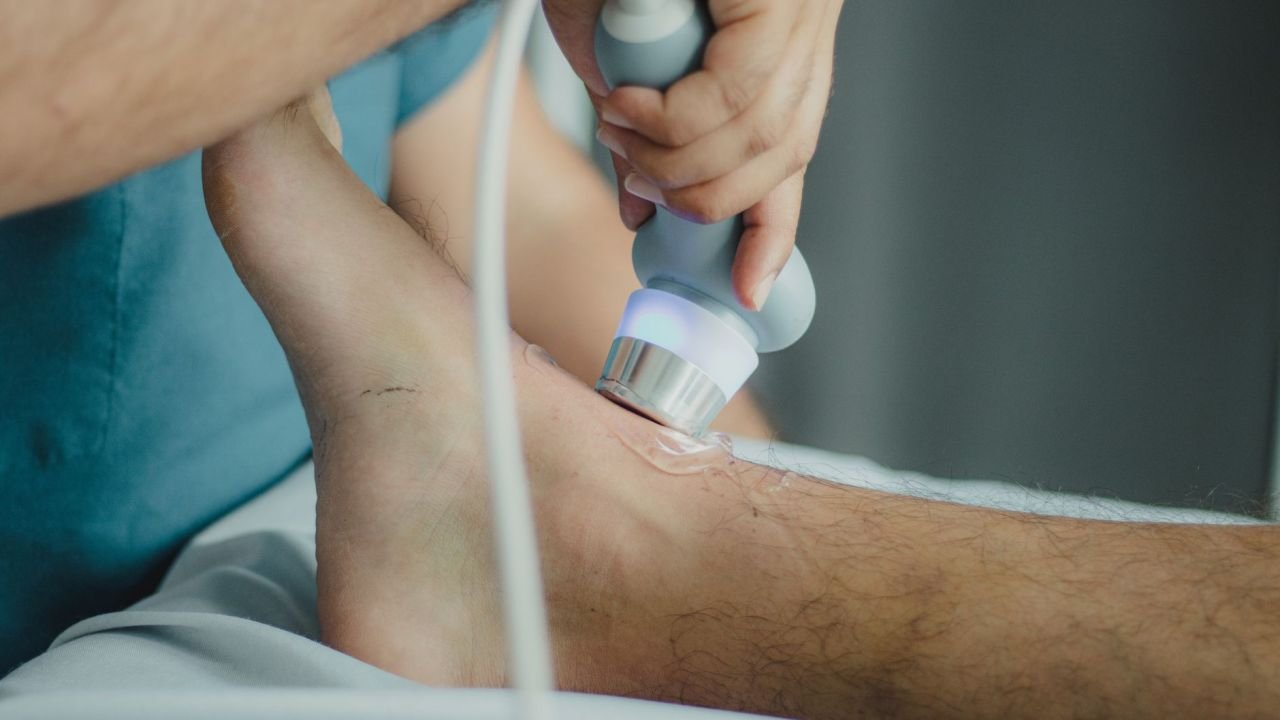A physiotherapist applying a therapy device to a patient's lower leg