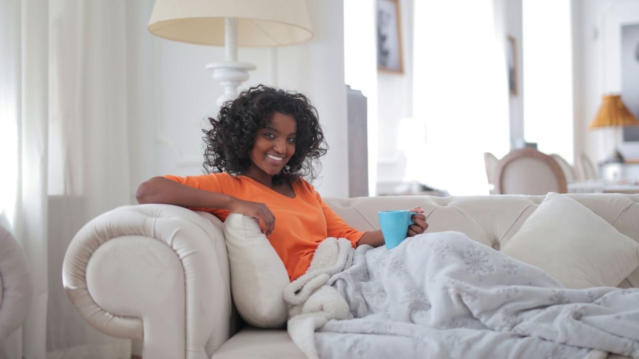 A woman wrapped in a blanket holding a mug at home